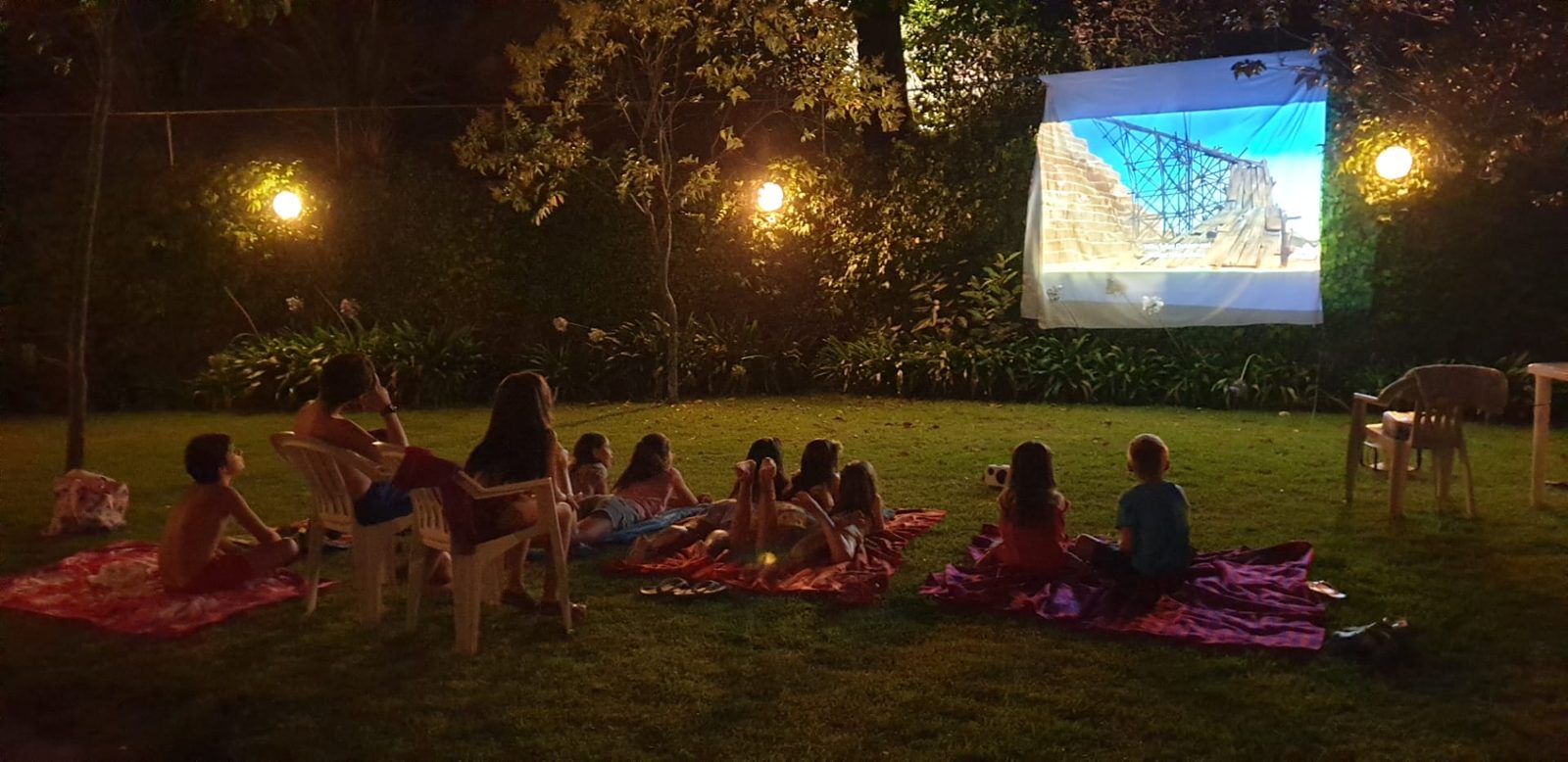 Crianças e jovens a ver um filme ao ar livre, numa noite de verão no jardim